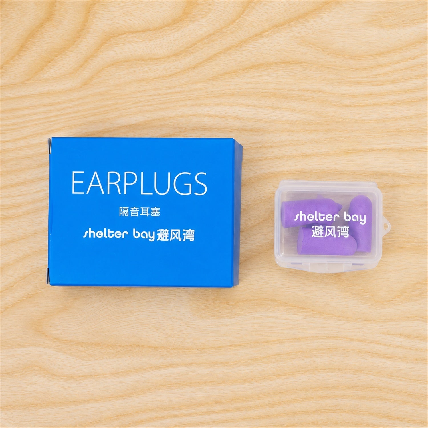 A blue box and a clear plastic case containing purple earplugs, both resting on a light wooden surface.