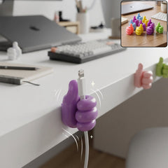 A purple thumbs-up clip holds a white charging cable to the side of a white desk, with other clips visible in the background.