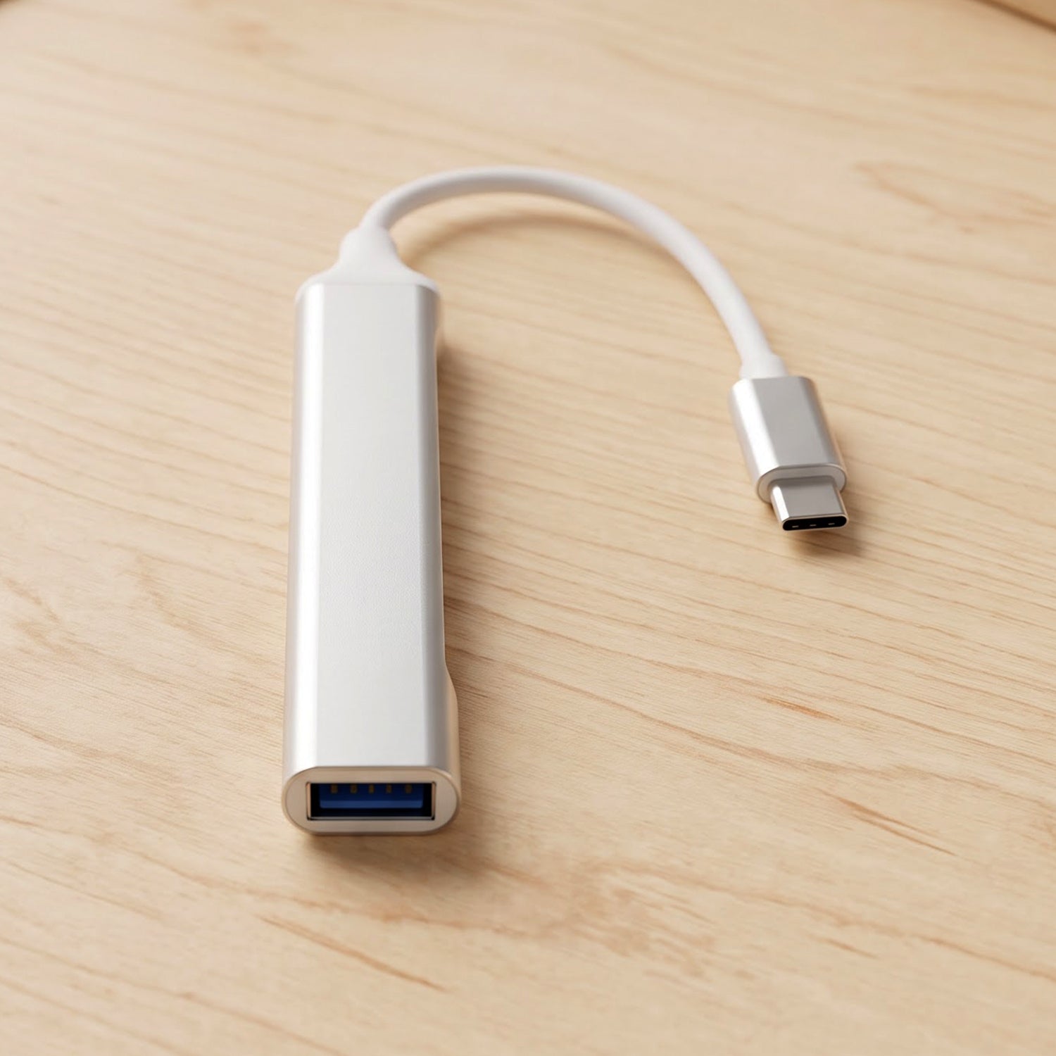 A silver Type C to four-port USB hub with a white cable and Type C connector resting on a light wooden surface.