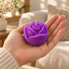 A purple rose-shaped candle rests in the palm of a hand, with a blurred living room in the background.