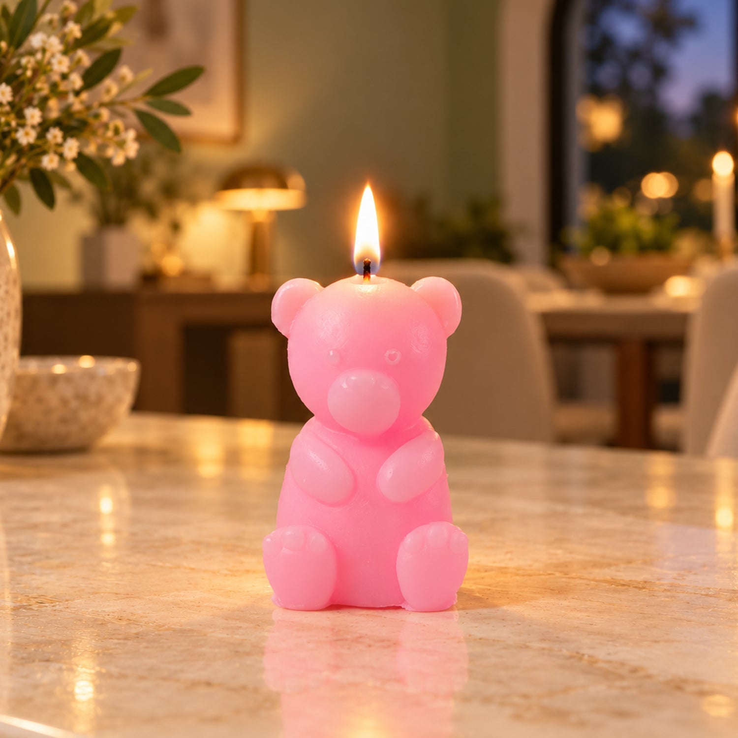 A lit pink teddy bear candle sits on a speckled countertop in a dimly lit room with blurred background lights.
