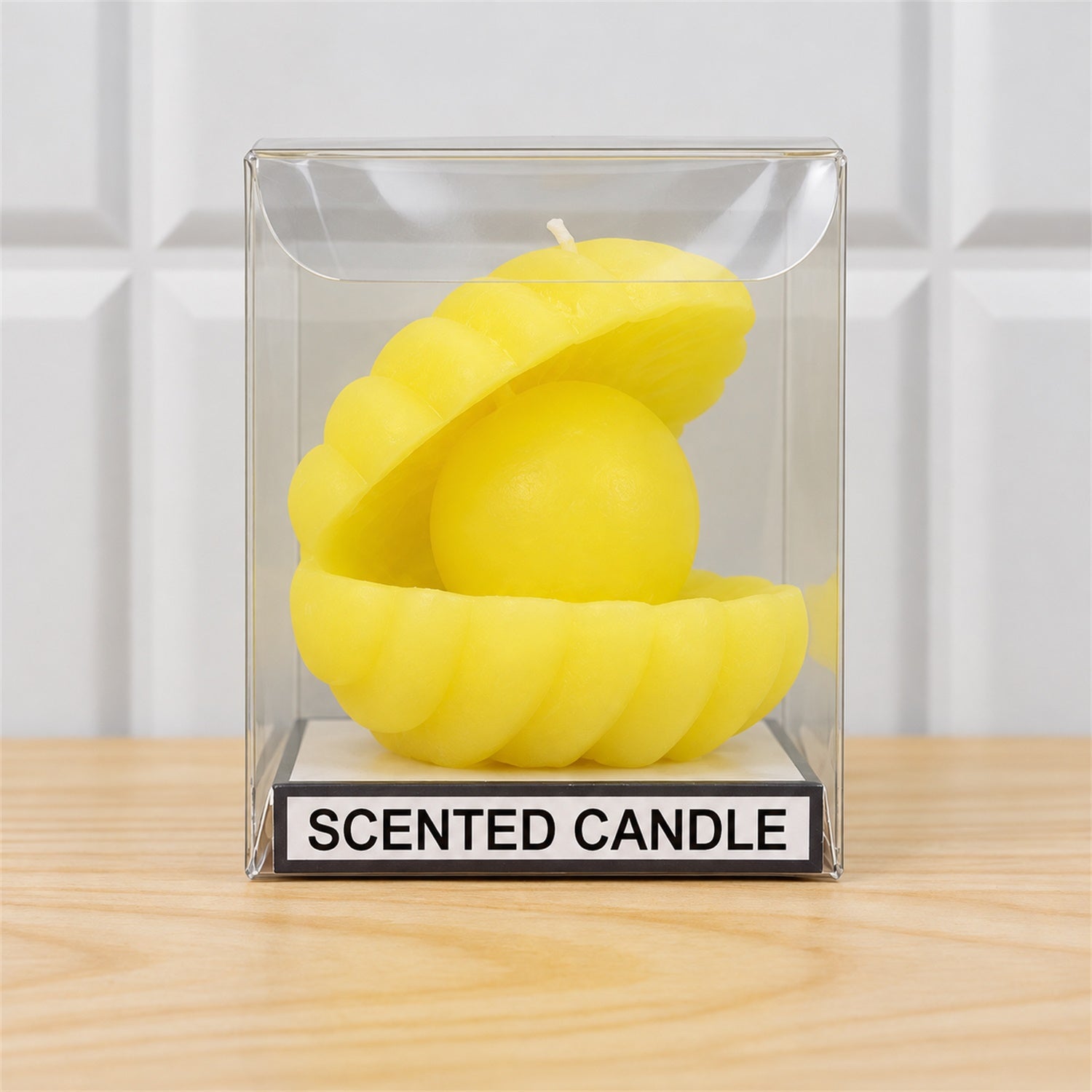 A yellow shell-shaped candle with a round center is displayed inside a clear plastic box on a wooden surface.