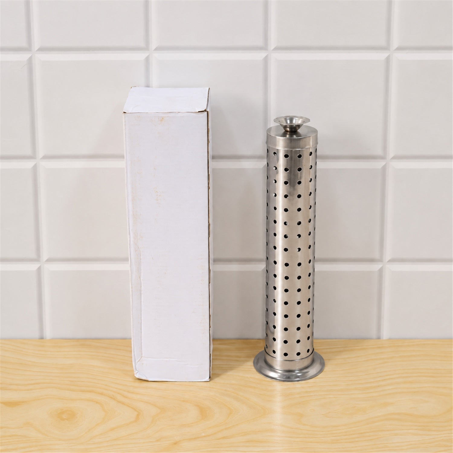 A silver perforated incense holder stands next to a plain white cardboard box on a light wooden surface, against a white