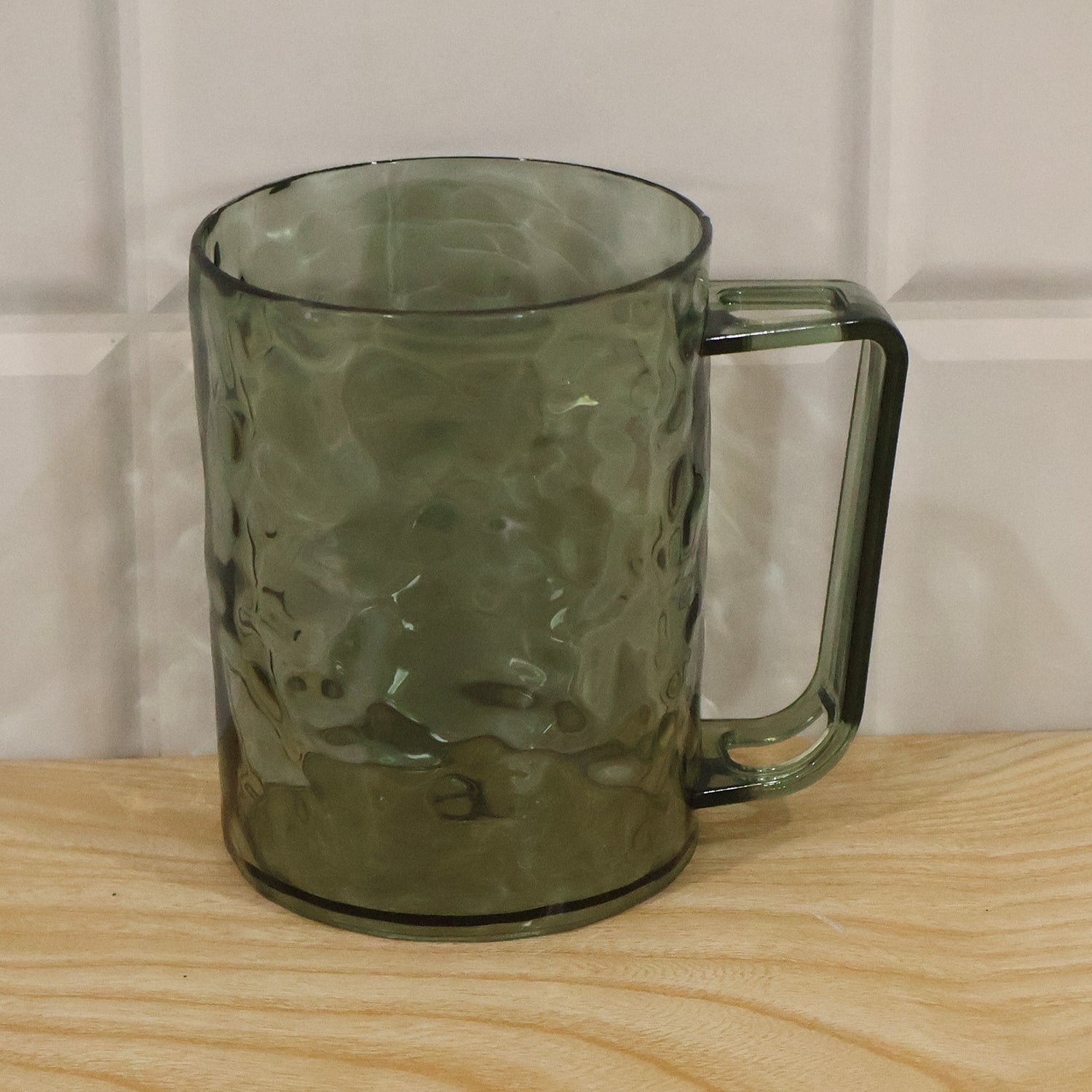 A dark grey textured plastic mug with a handle, sitting on a light wooden surface against a tiled wall.
