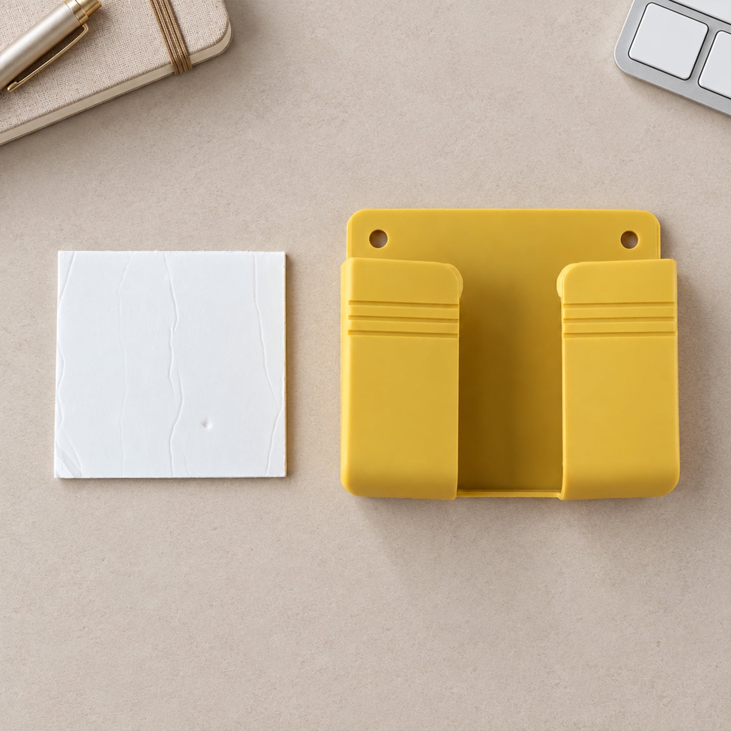 A yellow wall-mounted phone holder and a white adhesive pad on a neutral-toned surface.