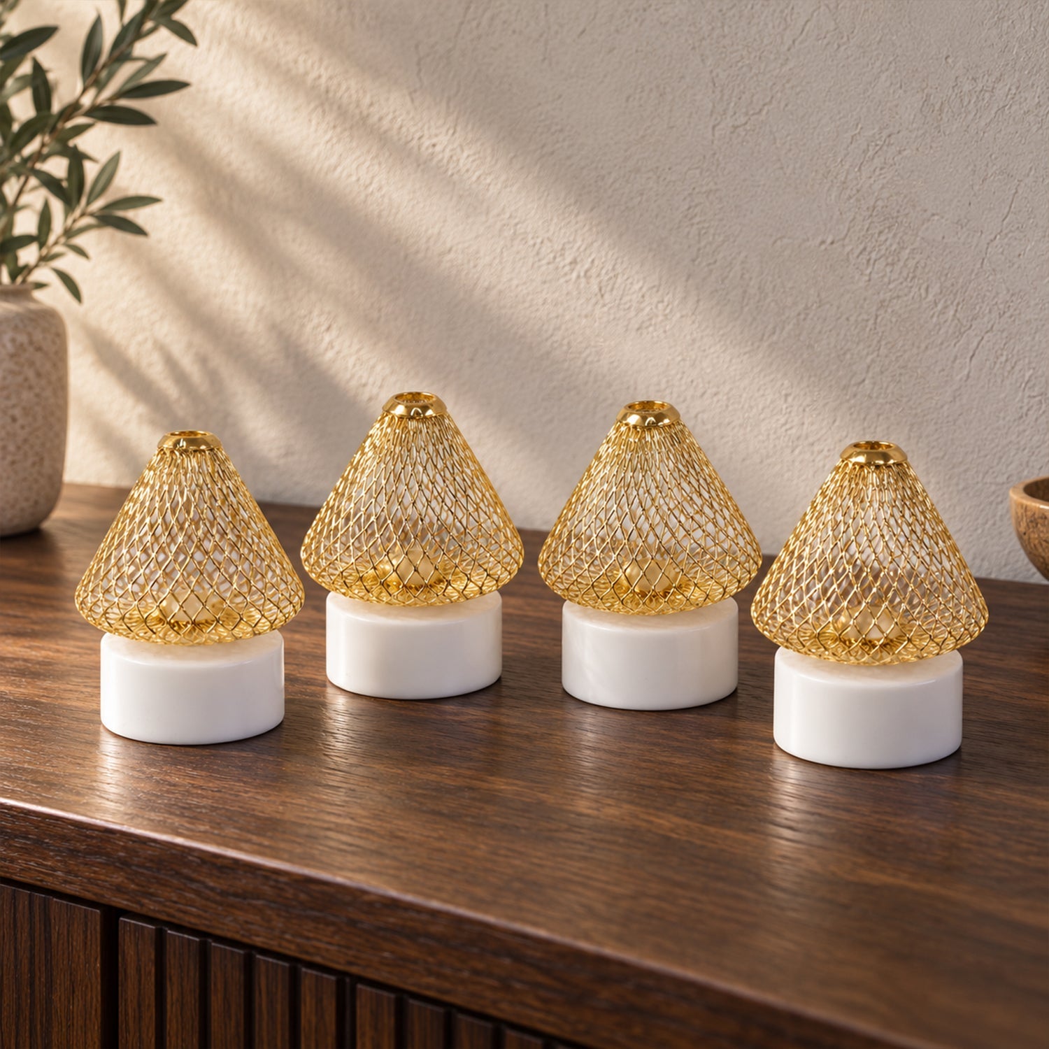 Four golden mesh LED lights with white bases sit on a dark wooden cabinet, with a plant in the background.