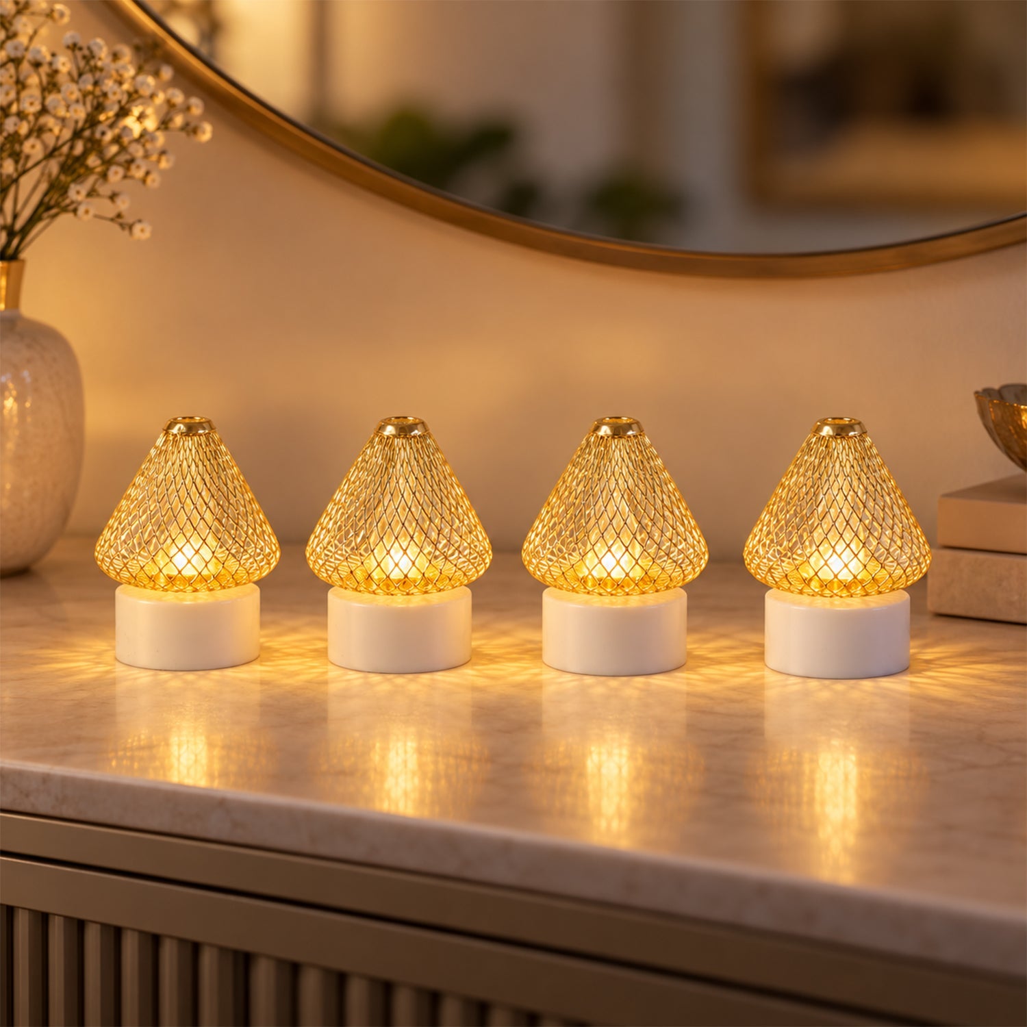 Four golden mesh LED lights with white bases cast a warm glow on a marble surface, reflecting in a round mirror.