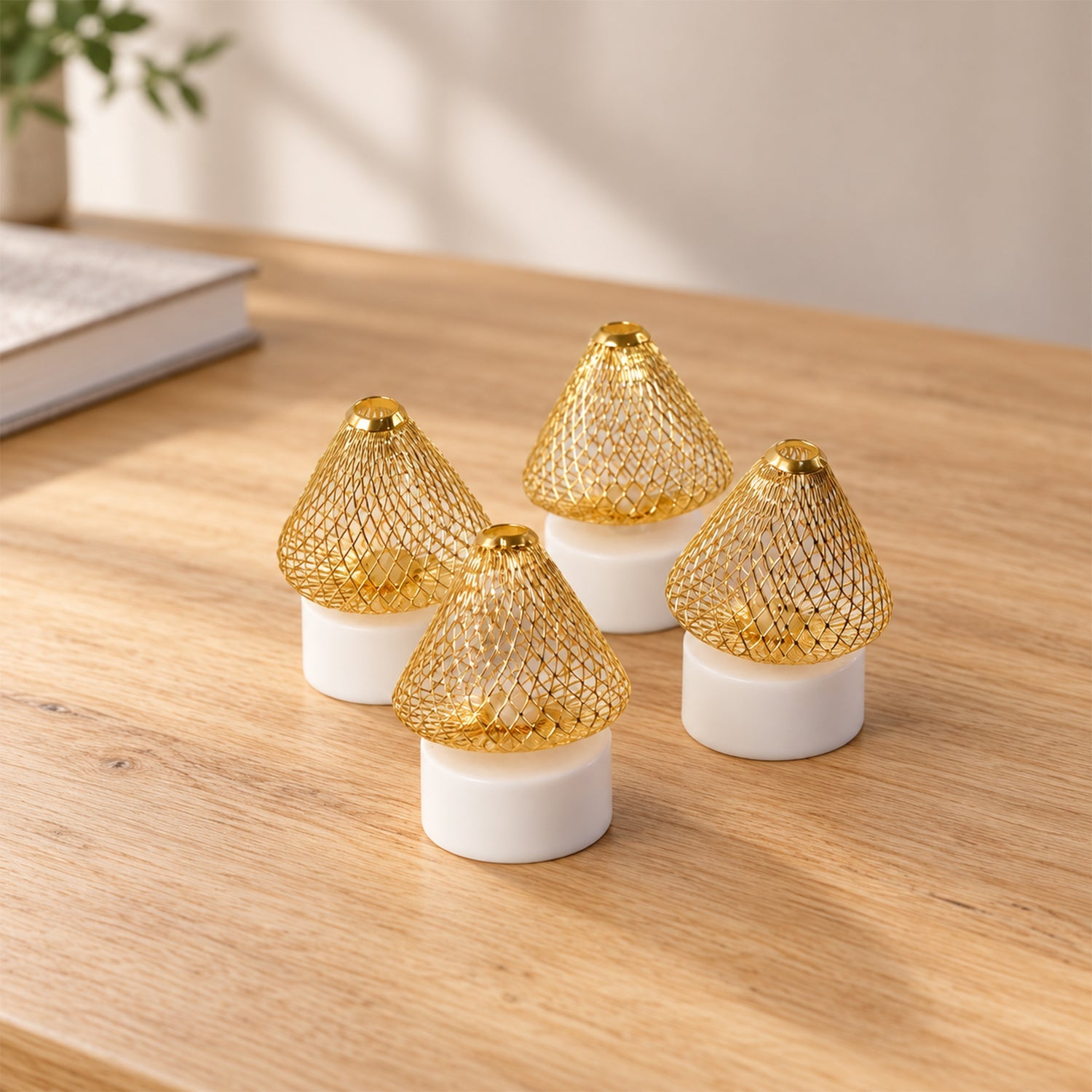 Four golden mesh LED lights with white bases are clustered together on a light wooden desk with a book and plant.