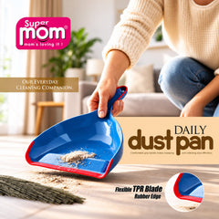 A person holds a blue and red dustpan with collected dirt, next to a broom on a wooden floor.