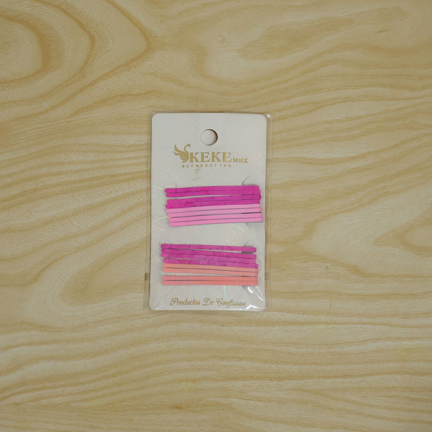 A pack of pink and magenta bobby pins on a white card, centered on a light wooden surface.