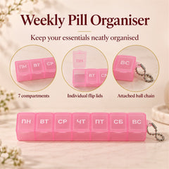 A pink plastic weekly pill box with seven compartments, each labeled with a Cyrillic day, on a light pink background with