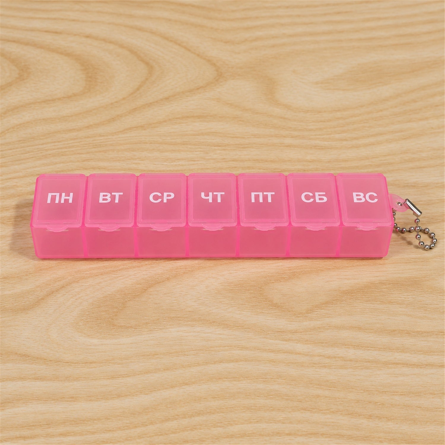 A pink plastic weekly pill box with seven compartments, each labeled with a Cyrillic day, with a silver ball chain â€“ view 9