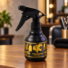 A black plastic spray bottle with a gold label featuring hair styling tools sits on a wooden counter.