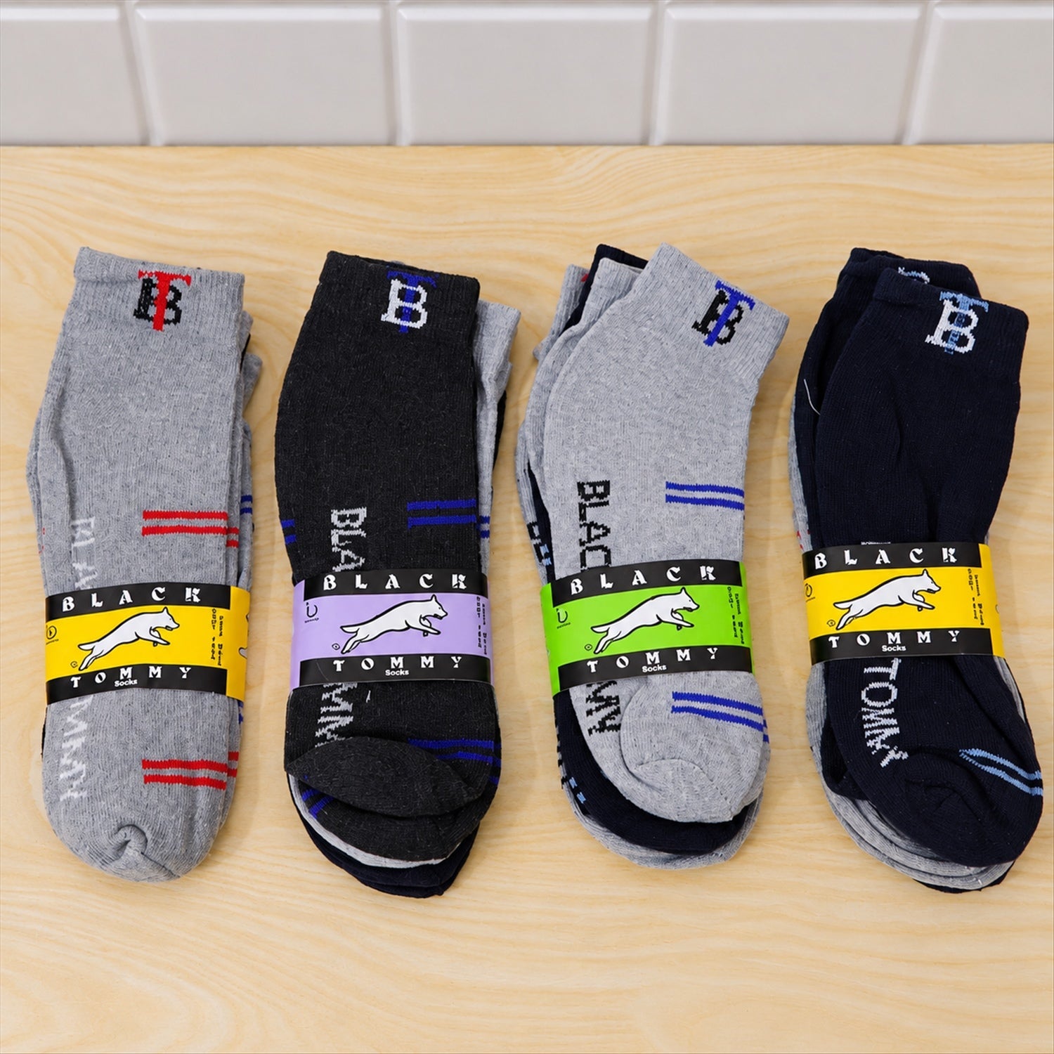Four bundled pairs of ankle socks, each with a branded label, are displayed on a light wooden surface.