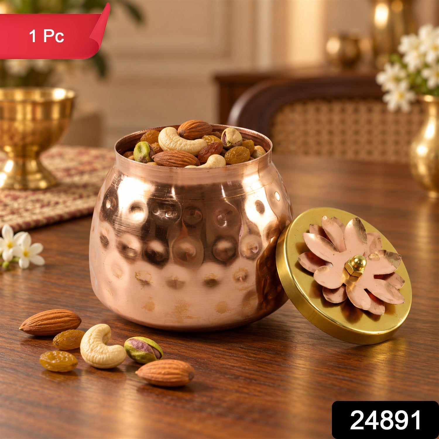 A hammered copper jar full of mixed nuts sits on a wooden table, with its gold and copper flower lid next to it. A red label