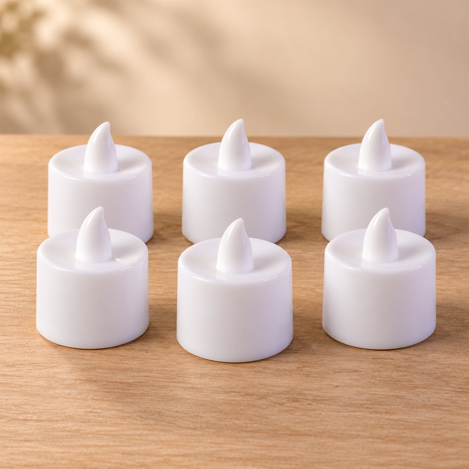 Six white flameless tealight candles are arranged in two rows on a light wooden surface, casting soft shadows.