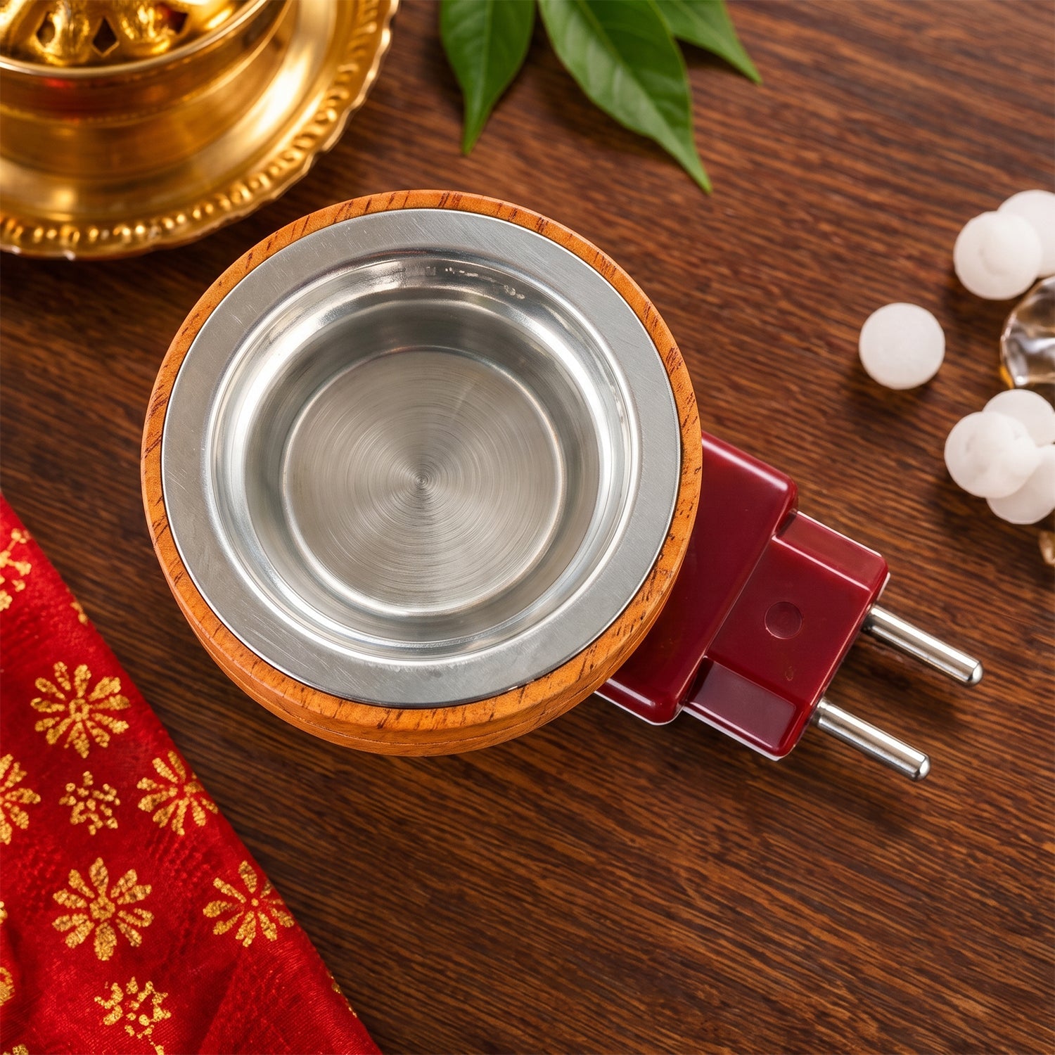Overhead view of a round wooden diffuser with a silver metal cup, next to a red fabric and camphor pieces.