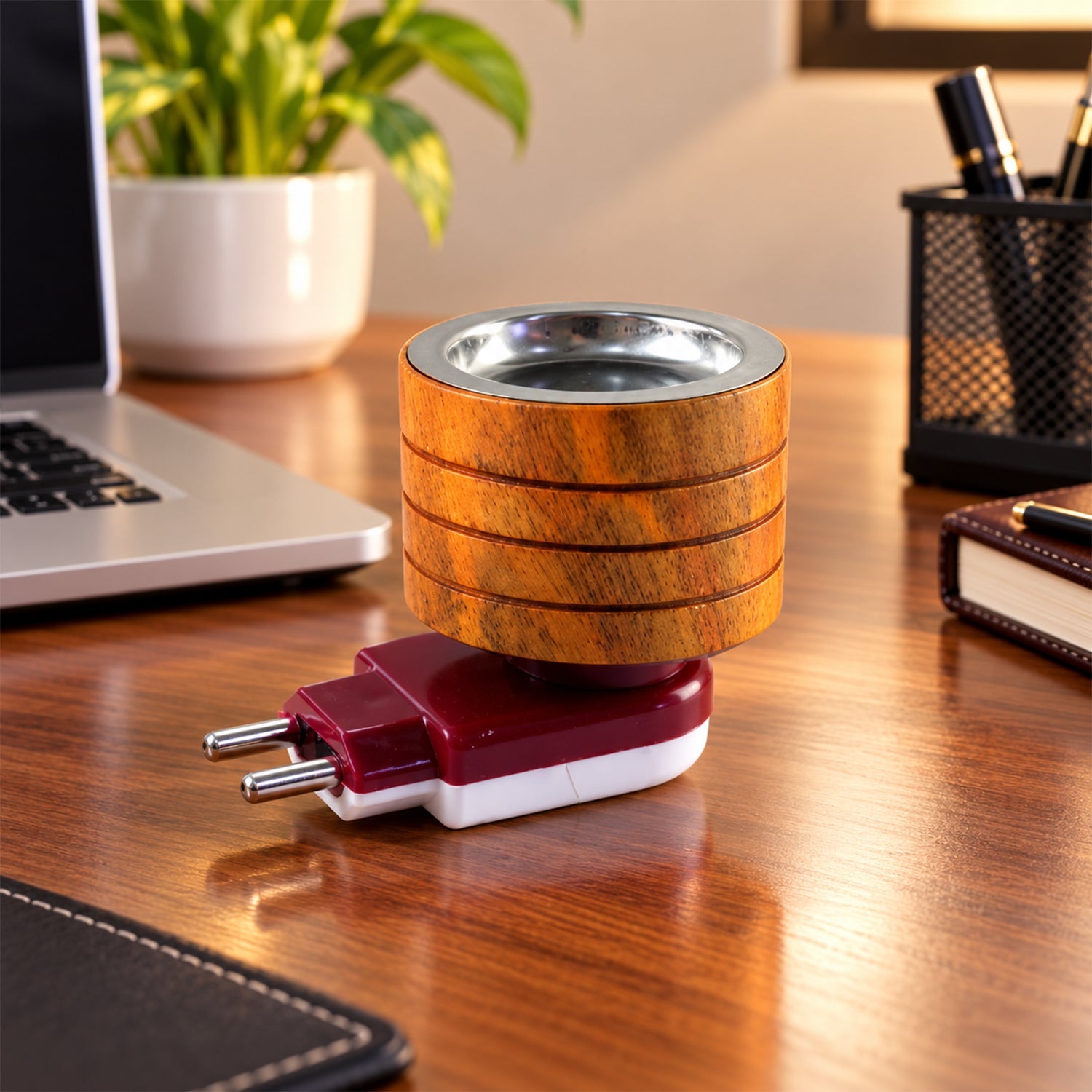 A wooden electric camphor diffuser rests on a wooden desk, surrounded by a laptop and office supplies.