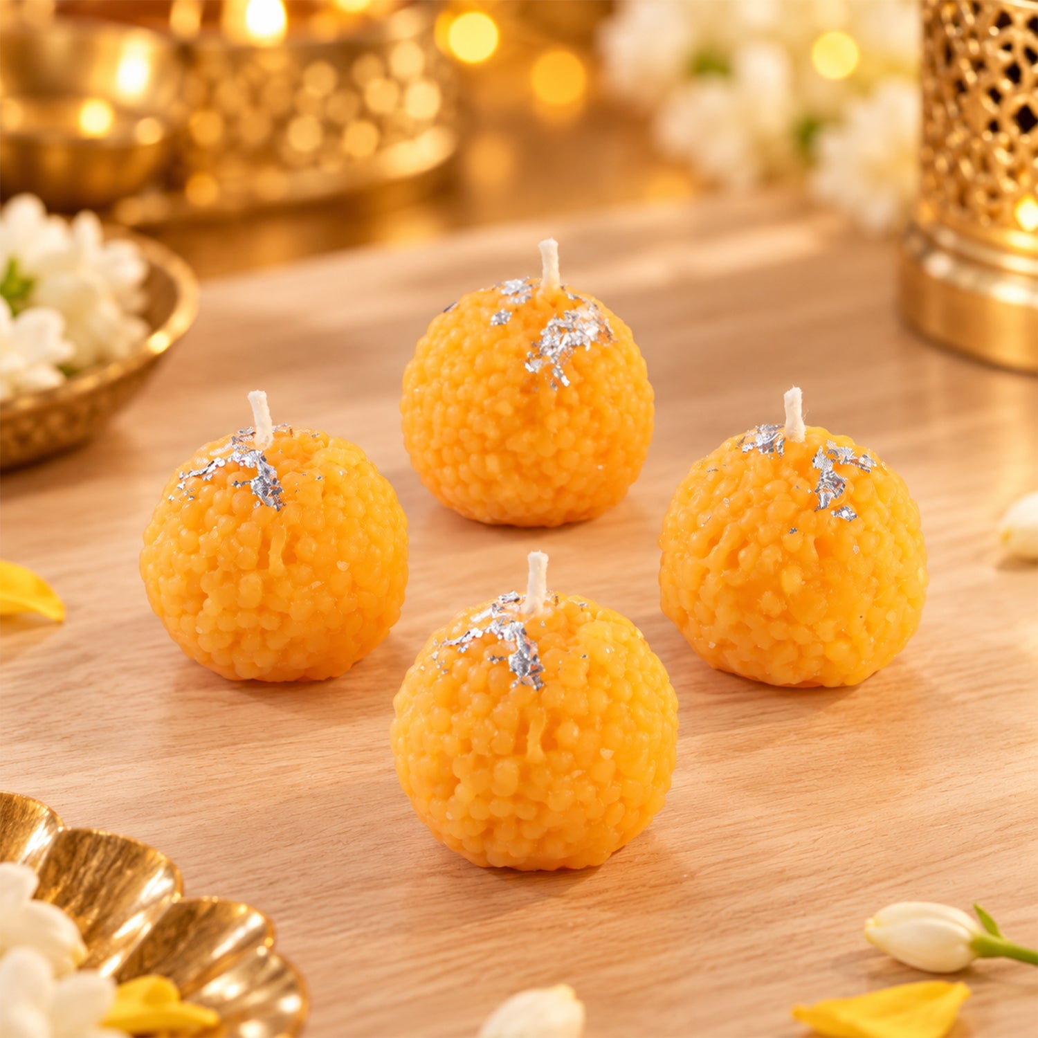 Four unlit orange spherical candles with silver flakes on a light wooden surface, with blurred decor.