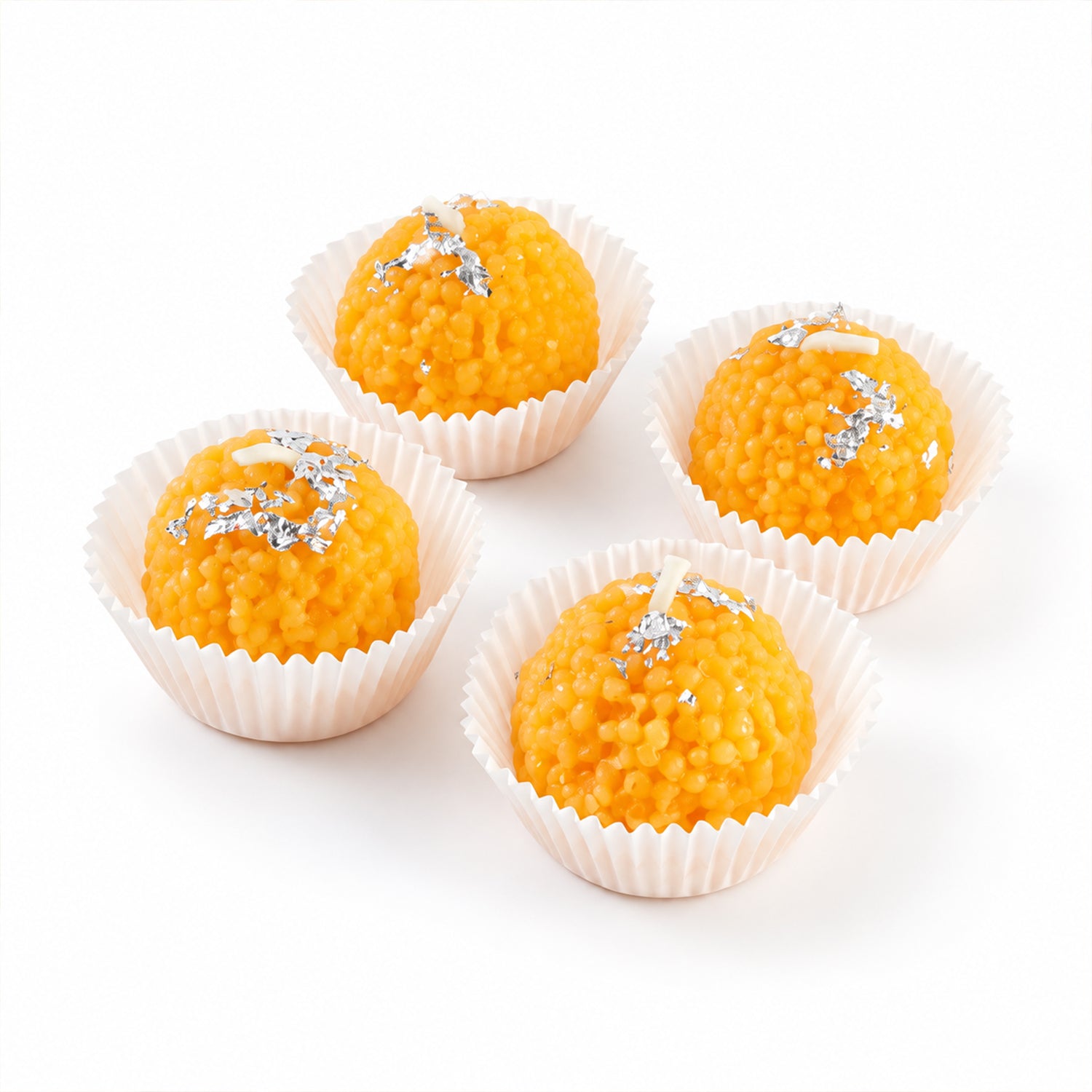 Four unlit orange spherical candles with silver flakes, each in a white fluted cup on a white surface.