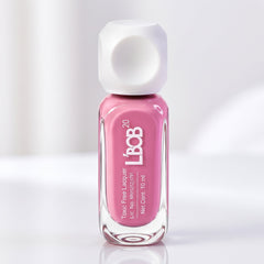 A pink nail polish bottle with a white cap stands upright on a reflective white surface, casting a subtle shadow.