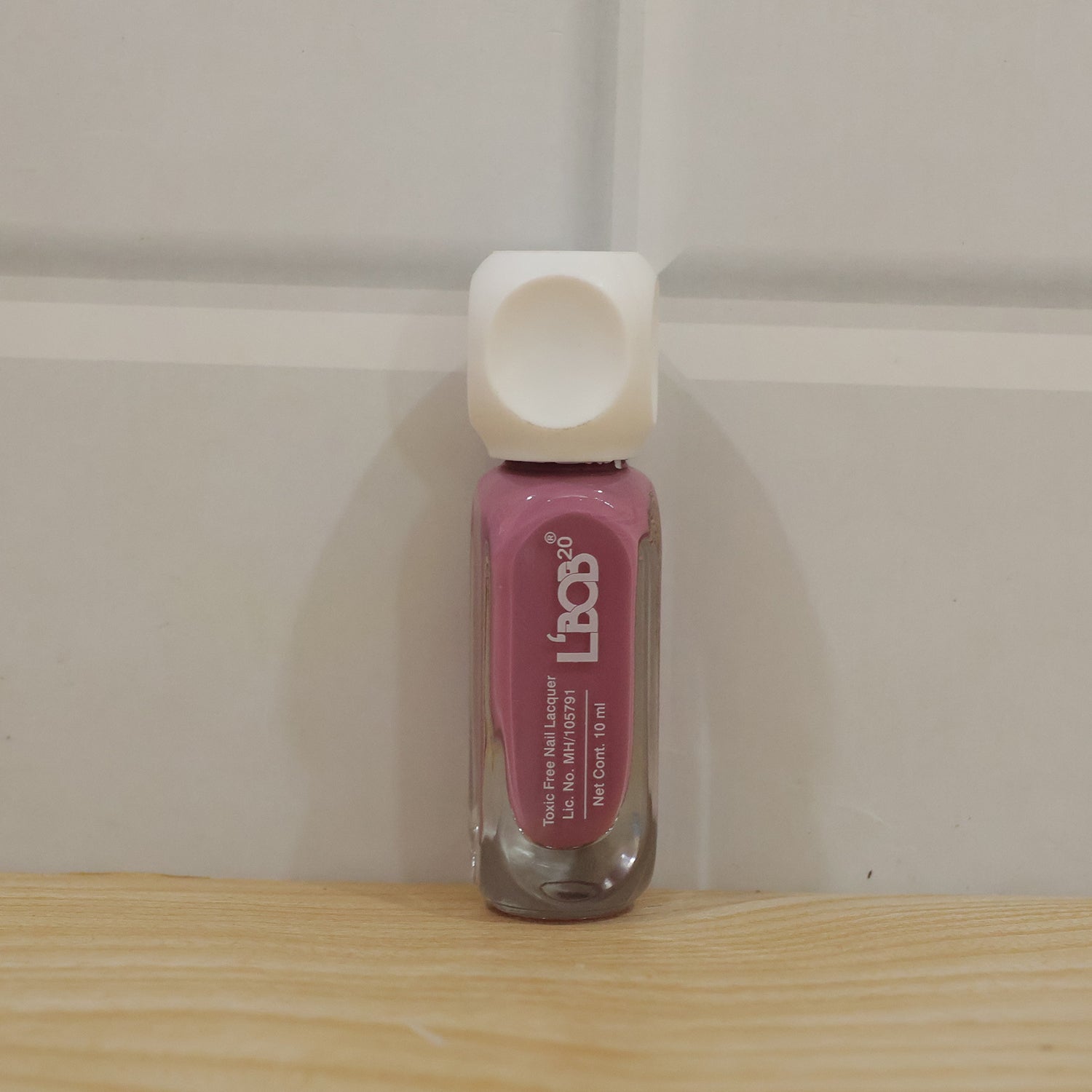 Hand holding mauve rose colour nail polish bottle during manicure