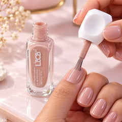 A hand applies nude pink nail polish to a fingernail, with an open bottle beside it.