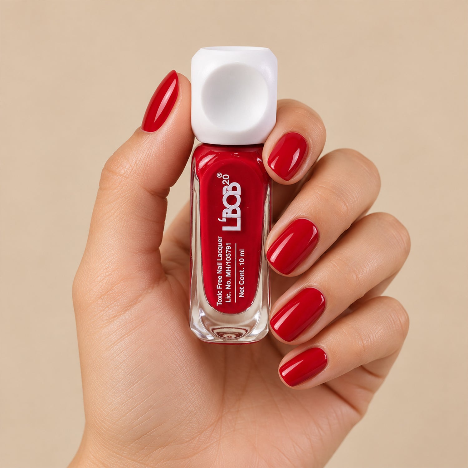 A hand holds a small clear bottle of red nail polish with a white square cap, against a light background.