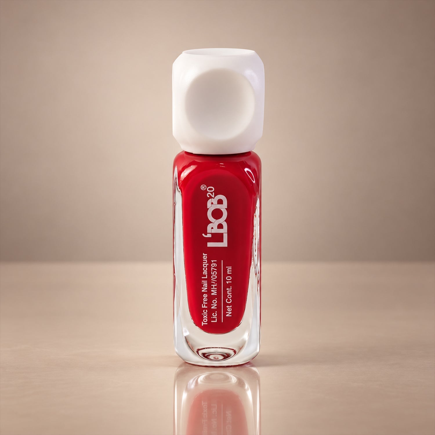A bottle of red nail polish with a white cap stands on a reflective surface against a beige wall.