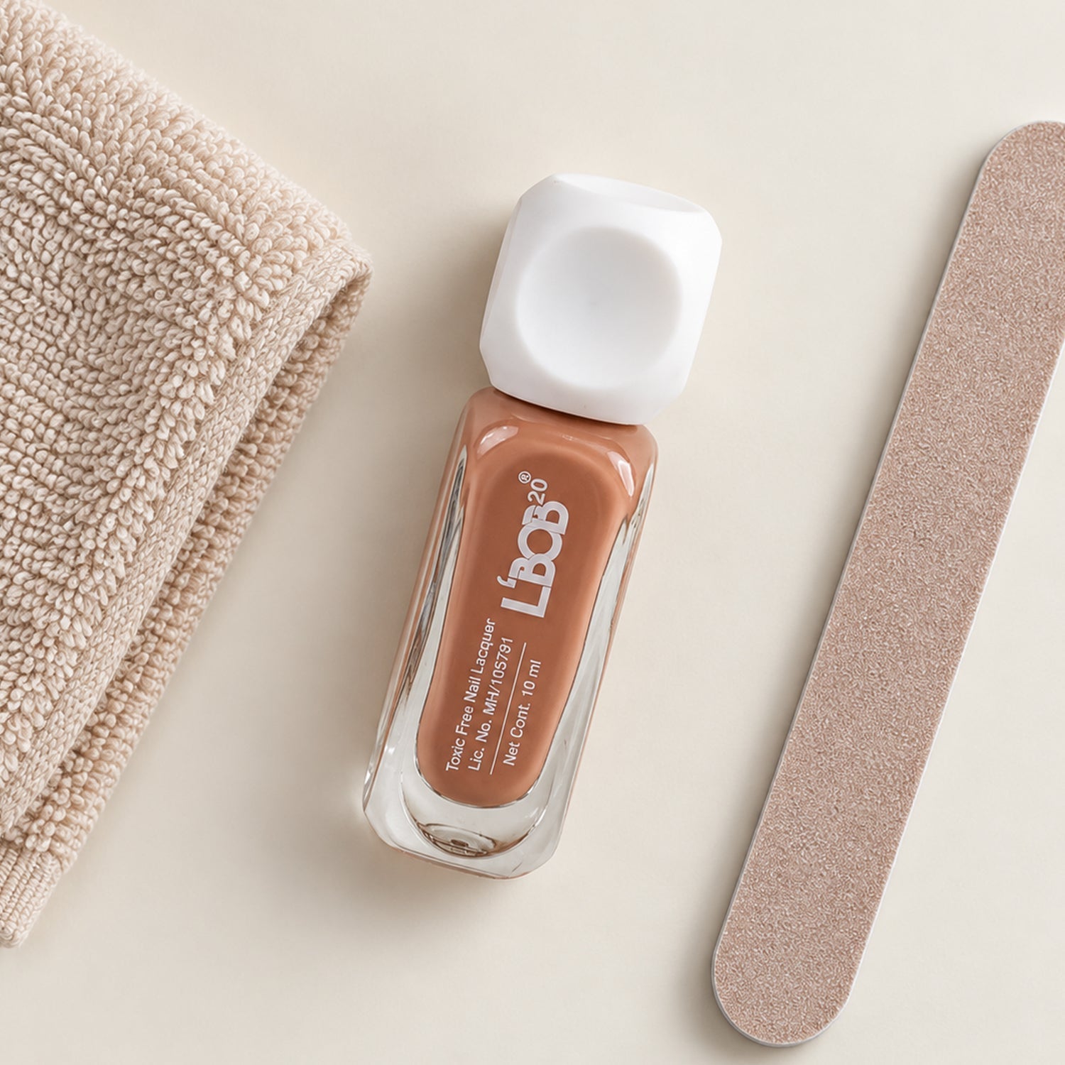 A small bottle of nude brown nail polish sits next to a beige towel and a nail file.
