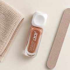 A small bottle of nude brown nail polish sits next to a beige towel and a nail file.