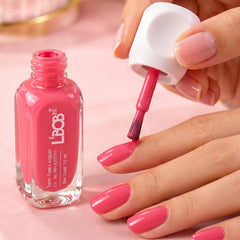 A person applies bright pink nail polish to their fingernails with a brush from an open bottle.