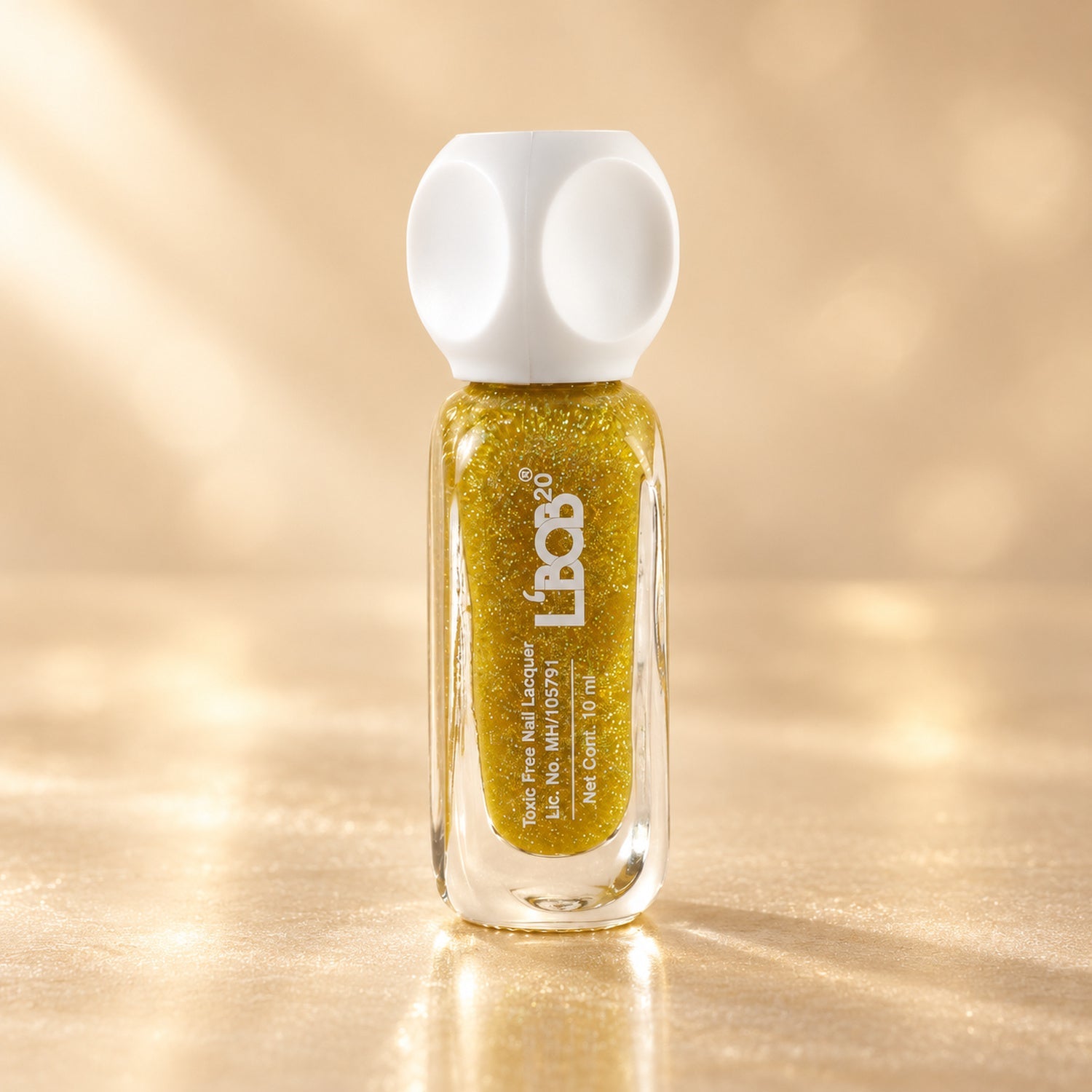 A bottle of gold glitter nail polish with a white cap stands on a reflective gold surface.