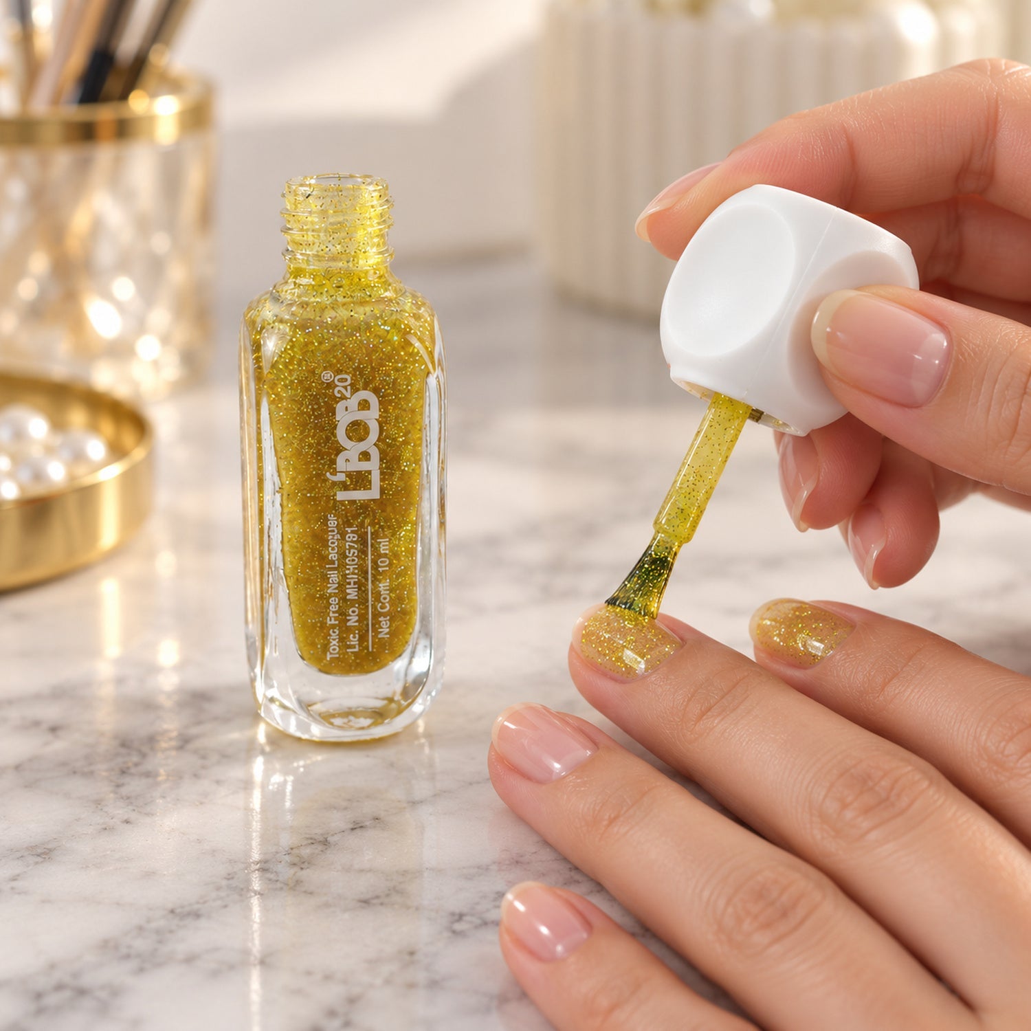 A person applies gold glitter nail polish to their fingernails, with a bottle of polish beside them.