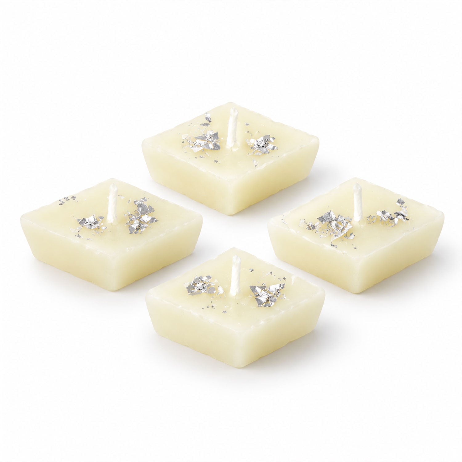 Four unlit diamond-shaped cream candles with silver foil accents are neatly arranged on a plain white background.