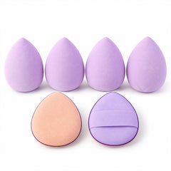 Four lavender teardrop sponges and two oval puffs, one peach and one purple, are neatly arranged.