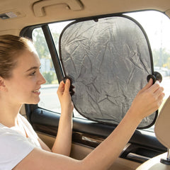 A woman installs a black foldable sunshade with suction cups on a car's side window, with a small inset showing two â€“ view 3