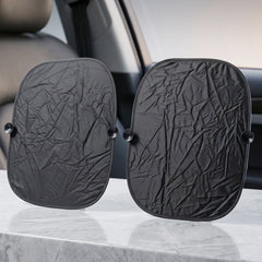 Two black foldable car sunshades with suction cups are displayed upright on a light-colored surface inside a car.