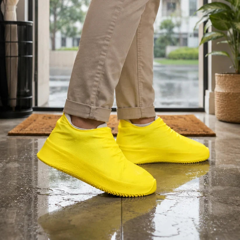 A person wearing khaki pants and bright yellow silicone shoe covers stands on a wet tiled floor near a doorway.