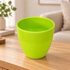 An empty, bright green plastic flower pot with a smooth finish sits on a light wooden table indoors.