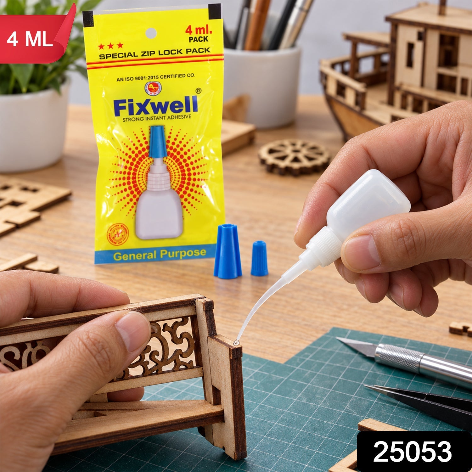 A person applies glue from a small white bottle with a fine nozzle to a wooden miniature structure. A yellow packet of