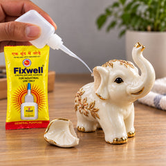 A hand applies glue from a white bottle with a fine nozzle to repair a broken ceramic elephant figurine.