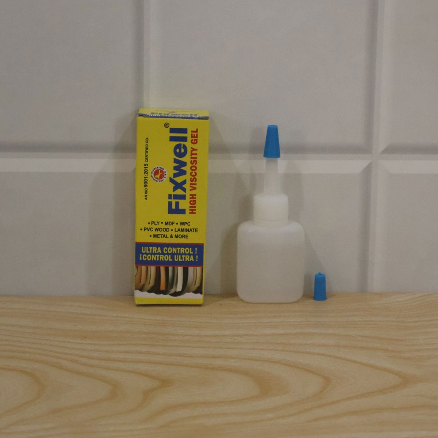 The Fixwell adhesive gel bottle and its yellow box are displayed on a light wooden surface against a white tiled wall.