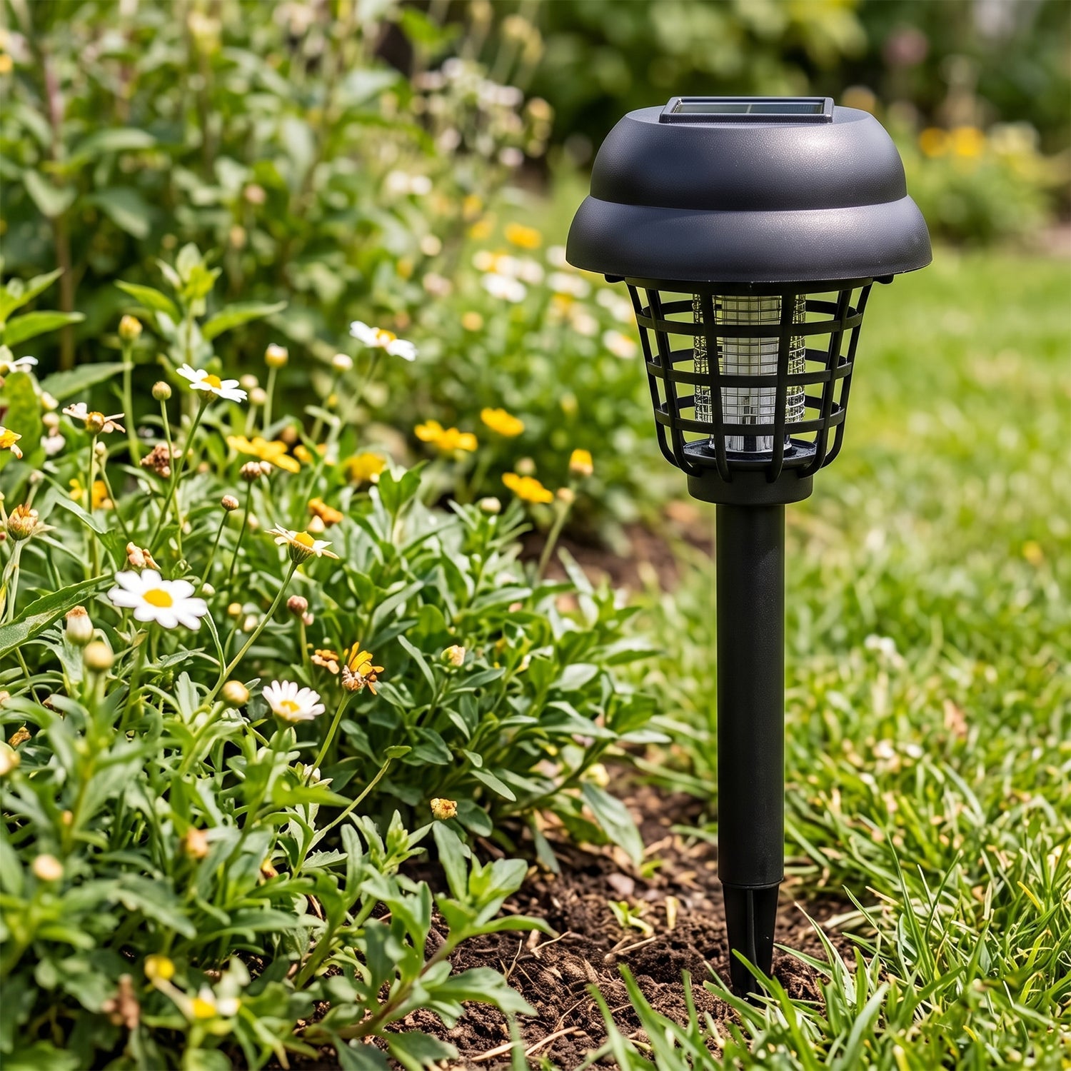 A black solar mosquito lamp is installed in a garden bed, surrounded by green foliage and small white flowers.