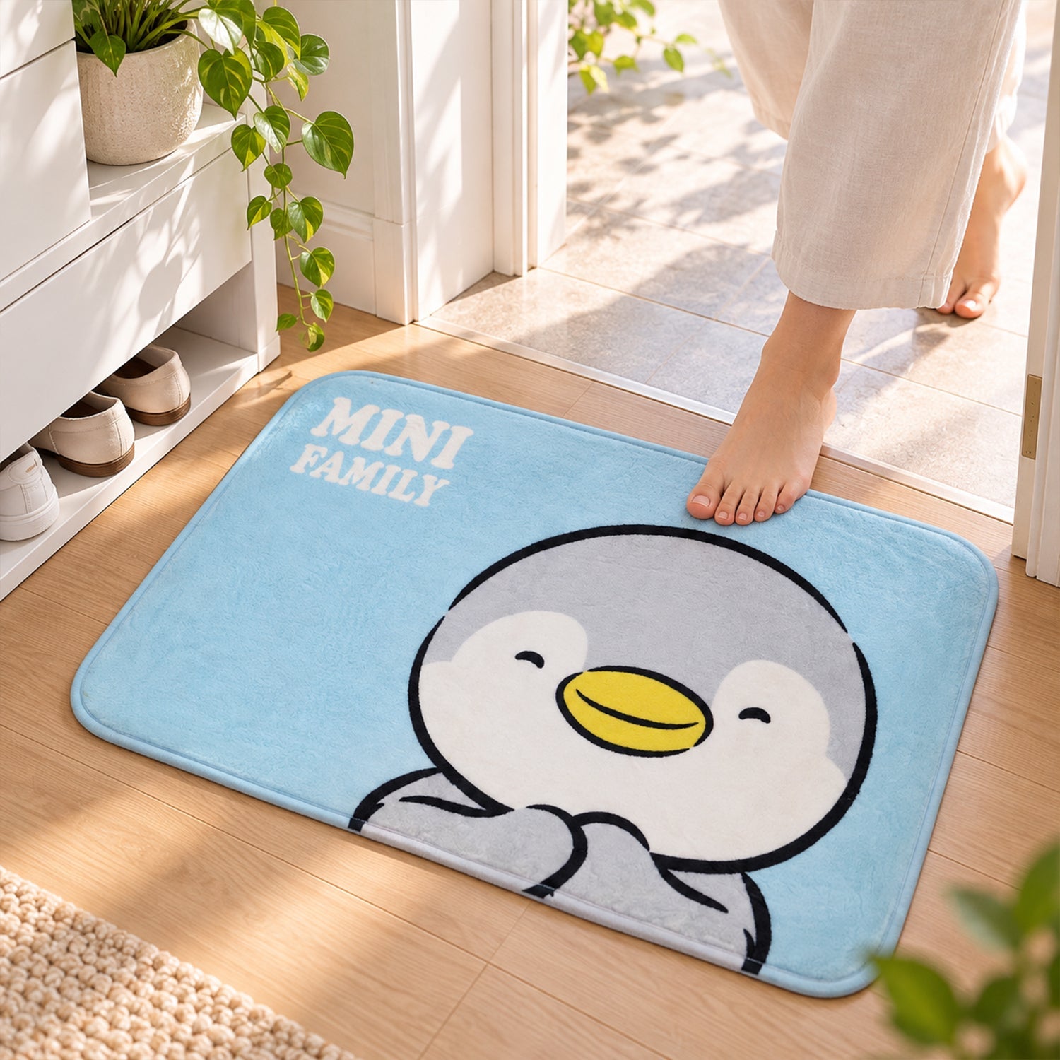 A person steps onto a light blue bath mat featuring a cute grey and white penguin design with yellow beak.