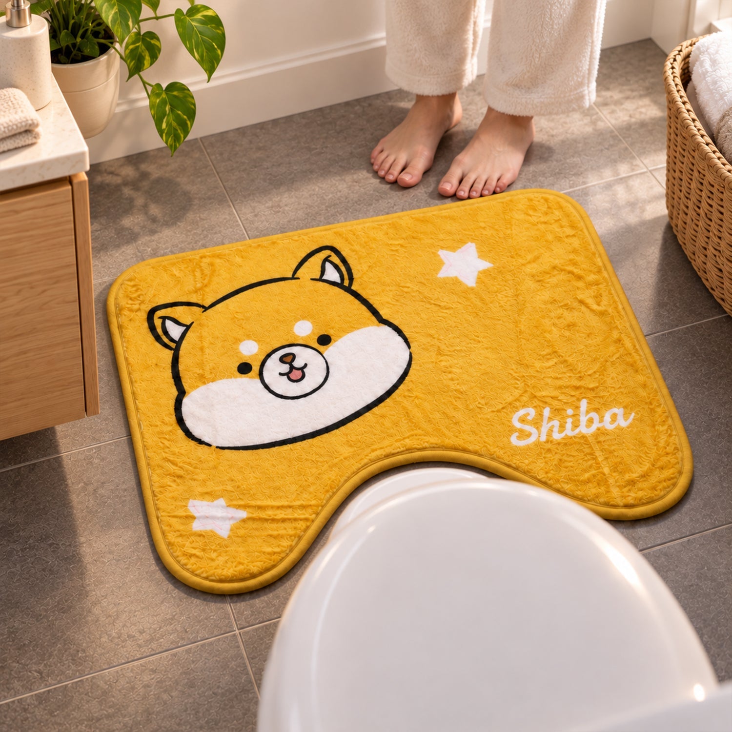 A person's bare feet stand on a grey tiled floor next to a yellow U-shaped toilet mat with a Shiba Inu character.