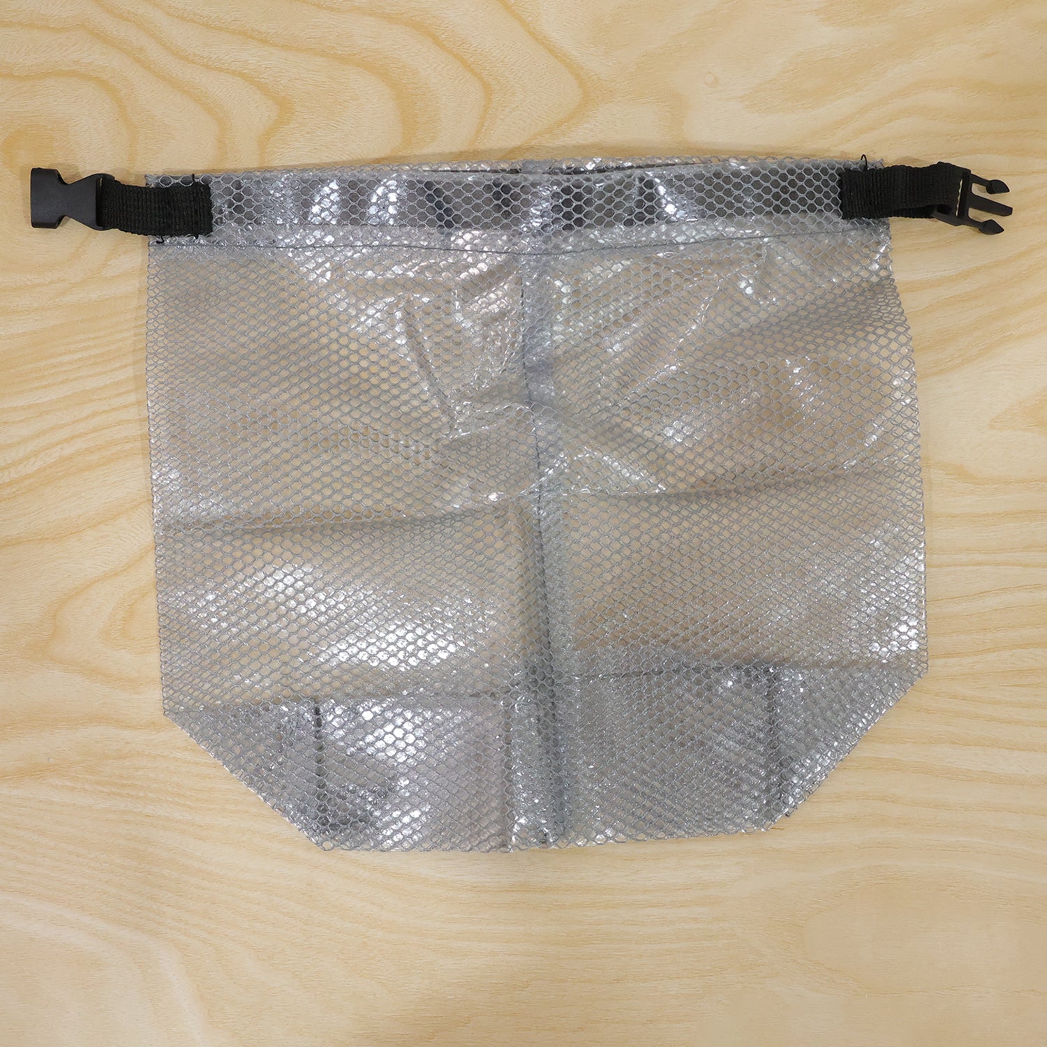 A flat grey mesh pouch with a black buckle and strap is displayed on a light wooden surface.