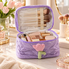 An open lavender quilted corduroy cosmetic bag with a pink and green tulip applique, filled with various makeup items on a