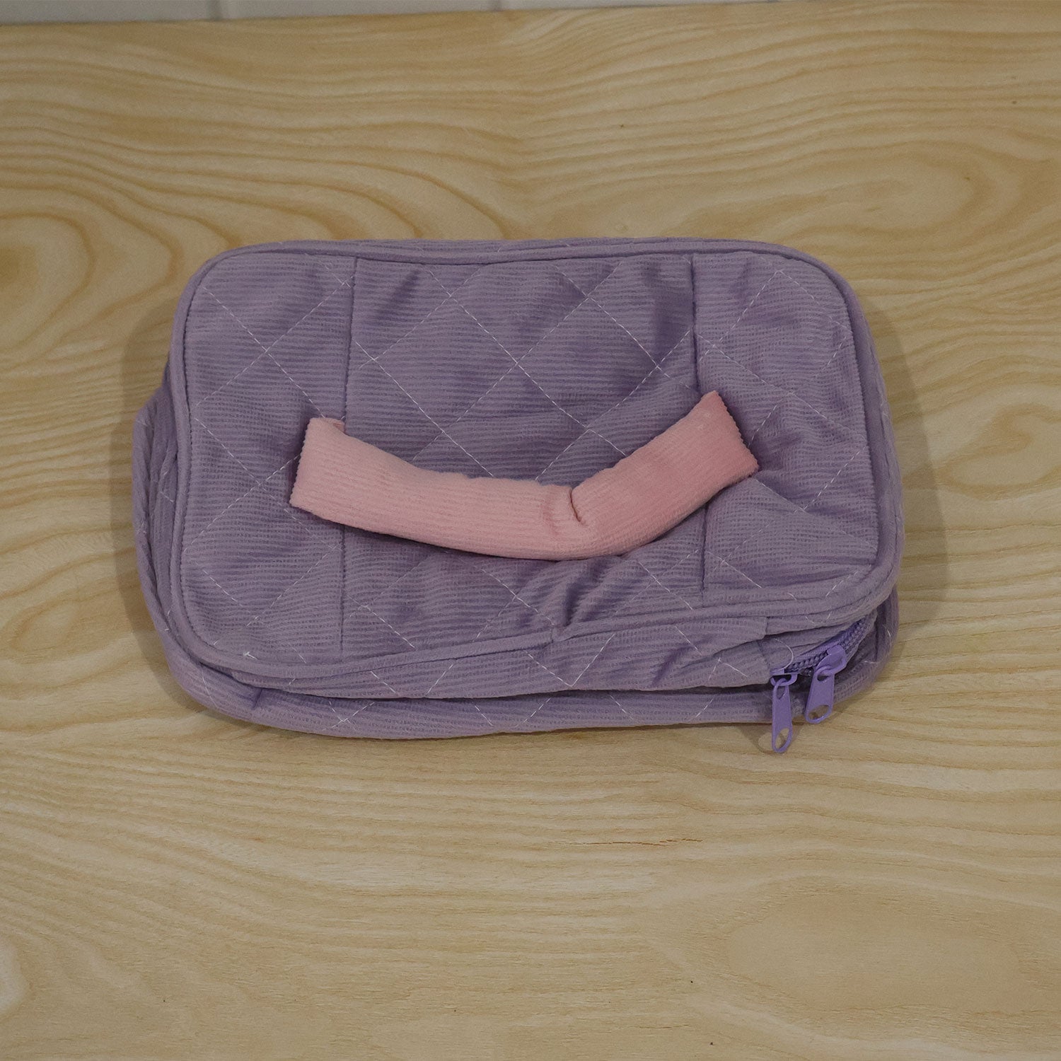 A closed lavender quilted corduroy cosmetic bag with a pink handle and a pink and green tulip applique, shown from a