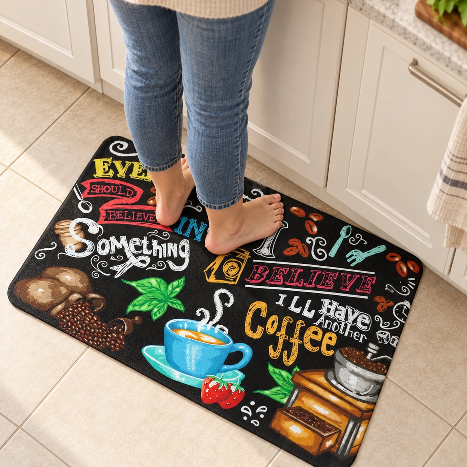 Bare feet standing on the black coffee-themed mat in a modern kitchen with white cabinets.